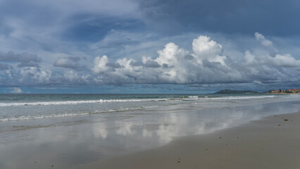A beautiful tropical beach during the day, without people. The waves of the turquoise ocean are foaming and spreading across the beach. Reflection on wet, smooth sand. The hotel building is far away.