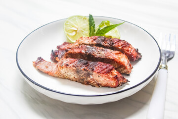 grilled fish slices and lime on a plate, with spoon and fork beside