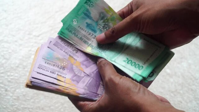 Man's hand is counting twenty thousand and ten thousand rupiah banknotes