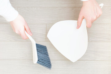 Female hands sweeping the floor with a brush and dustpan top view close-up.