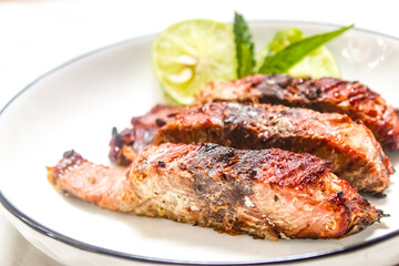 close up of grilled fish slices and lime on a plate, with a spoon and fork beside it