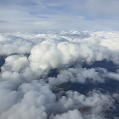 Expansive view from an airplane window showcasing a sea of white, fluffy clouds against a blue sky. The ethereal atmosphere captures the beauty of flight and serene skies.