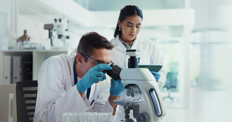 Obraz premium Scientist, woman and man with microscope for biotech, testing and medical research. Chemistry, laboratory and assistant with tablet report for pharmaceutical or pathology experiment for breakthrough