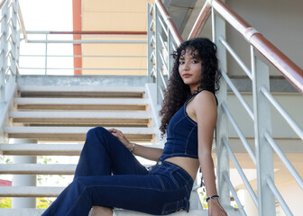 Curly-haired model wearing blue jeans and chains sitting on the stairs