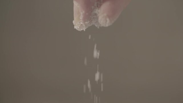 Close up slowmotion shot of a male hand dropping some salt on top of baking flour while moving his fingers LOG