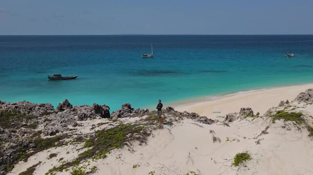 Male traveler exploring a desert island.Standing on a hill and looking into the distance of the Indian Ocean.Yaght at background
