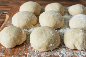 Raw dough balls with flour on wooden cutting board. Close up.