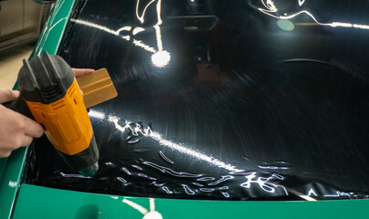 Applying tinting foil on a car window in the tuning studio close-up. Male car service worker glue...
