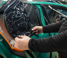 Applying tinting foil on a car window in the tuning studio close-up. Male car service worker glue...