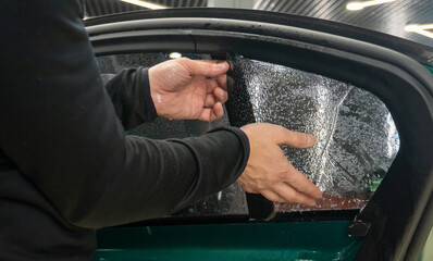 Applying tinting foil on a car window in the tuning studio close-up. Male car service worker glue...