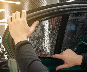 Applying tinting foil on a car window in the tuning studio close-up. Male car service worker glue...