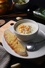 a bowl of corn soup on a white plate with a slice of bread
