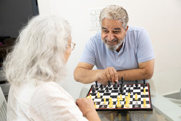 happy senior indian couple enjoying a game of chess while smiling and engaging in a friendly...