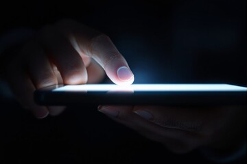 Close-up of a hand touching a glowing smartphone screen in the dark.