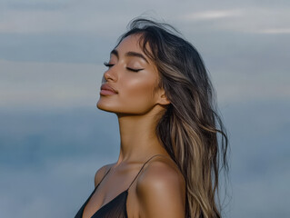 Naklejka premium Woman with long hair enjoying a serene moment by the ocean under soft clouds