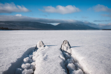 Pair of cross country skis in fresh snow on lake with mountains, Maine