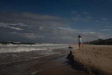 Profile Young girl walking down beach moody sky