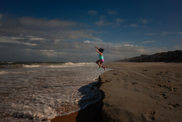 Side view young girl jumping into ocean waves blue sky