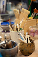 Assorted pottery tools in ceramic cups on a studio workspace