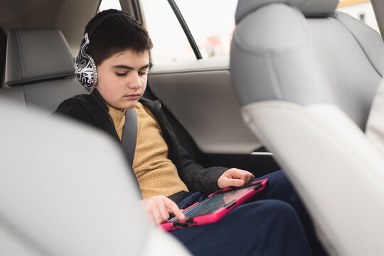 Teen boy with headphones on in car plays on electronic device