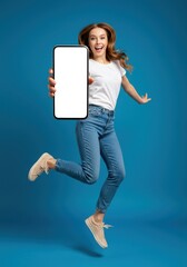 A cheerful caucasian woman in casual clothes jumps with excitement, holding a large smartphone with a blank screen blue background 02