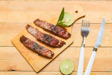  grilled fish slices and lime on a chopping board on a wooden table, with spoon and fork beside