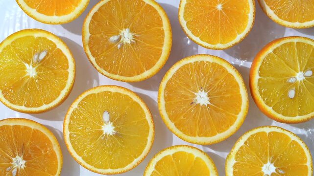 Close up video of mandarin slices surrounded by water ripples. White background with half oranges placed on water waves.