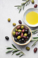 Bowl of assorted olives with olive oil and olive branches on marble background