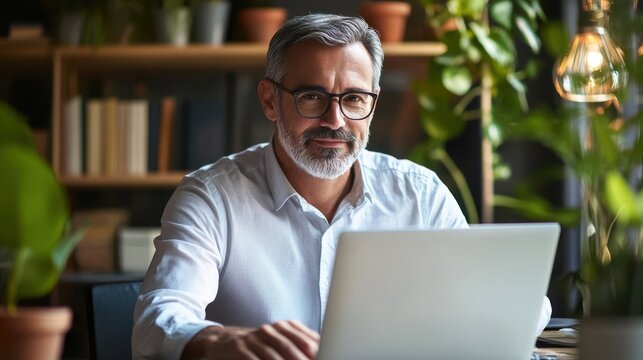 Mature business man executive manager looking at laptop computer watching online webinar training or having virtual meeting video conference taking notes, doing market research working in office.