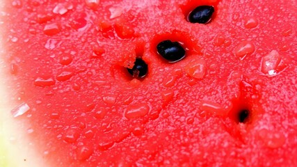 A close-up of a juicy watermelon slice, showing the vivid red pulp with black seeds and moisture glistening on the surface.