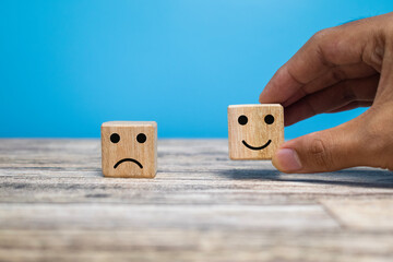 male hand putting happy face and sad face expression emoji on wooden block isolated on blue background