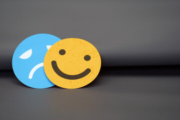 Sad face emoticon hiding behind a smiling face, the concept of duality of emotions, mood swings,...