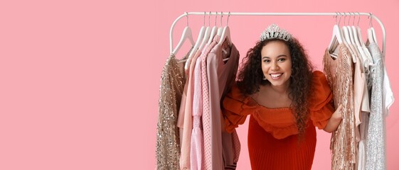 Beautiful African-American girl near rack with prom dresses on pink background with space for text © Pixel-Shot