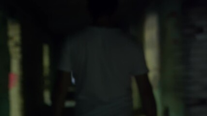 Lone tourist wandering through decaying urban structure, moving cautiously inside dimly lit hallway with faded weathered walls, embodying urban exploration mystery. Light flashing