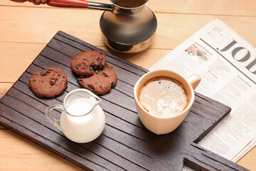Board with cup of coffee, milk, cookies and cezve on light wooden background, closeup