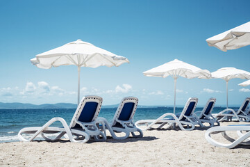 Weekend at sea. Relaxing summer beach with sun loungers and umbrellas by the calm sea