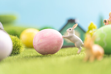 There is a cute bunny that is gently pushing a pink egg in the grass