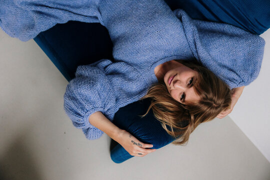 Woman in a blue knit dress relaxing on a stylish blue sofa.