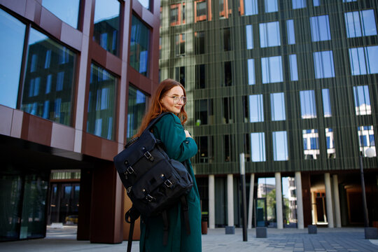 Girl student standing near modern university building and smiling