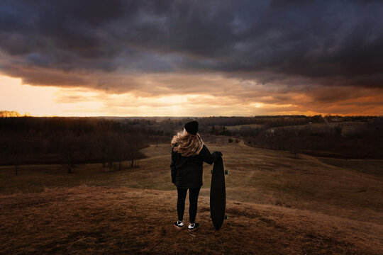 Teenage girl standing with skateboard dramatic sky