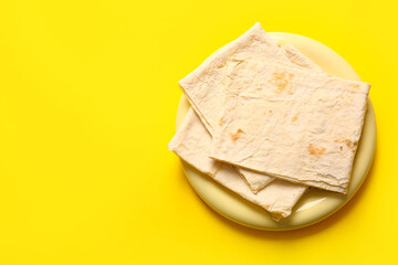 Plate with fresh thin lavash on yellow background