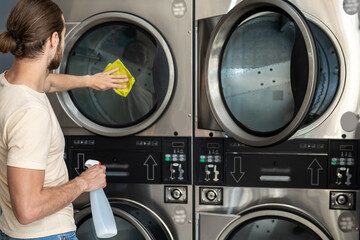 Male cleaning washing machine and dryer in laundromat