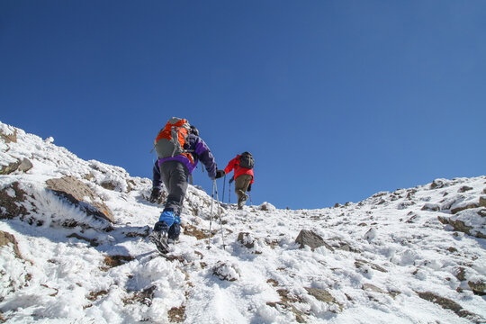 Tourists ascend Mount Aragats in Armenia during late spring or early summer, trekking through snowy and rocky terrain under a bright blue sky. A scenic adventure in the Caucasus Mountains