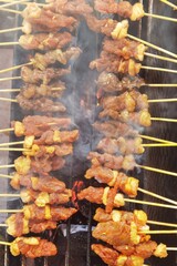 Grilling pork satay on stove with fire from charcoal, popular tasty street food in Thailand