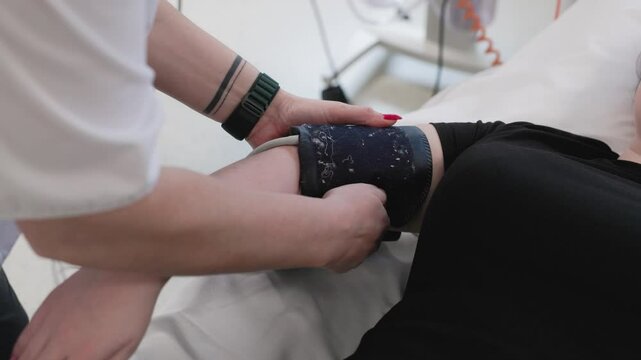 A nurse checks a patient's blood pressure using a Philips cuff in a hospital setting. The patient's arm is extended, and the healthcare worker's hands secure the device
