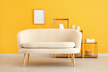 Cozy white sofa and shelving unit with frames near yellow wall