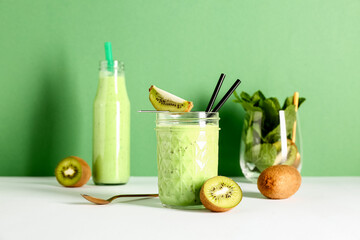 Glass and bottle of fresh kiwi smoothie with mint on white table