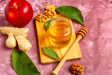 Wooden board with jar of sweet honey, walnut, ginger and apple on purple background