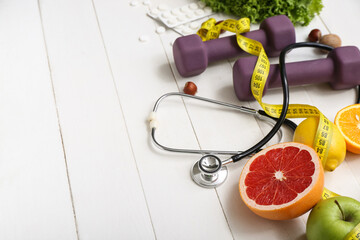 Composition with healthy products measuring tape, dumbbells and stethoscope on white wooden...