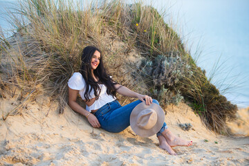 Latin woman, brunette, young and beautiful, lying on a fine white sand dune. She is dressed in...